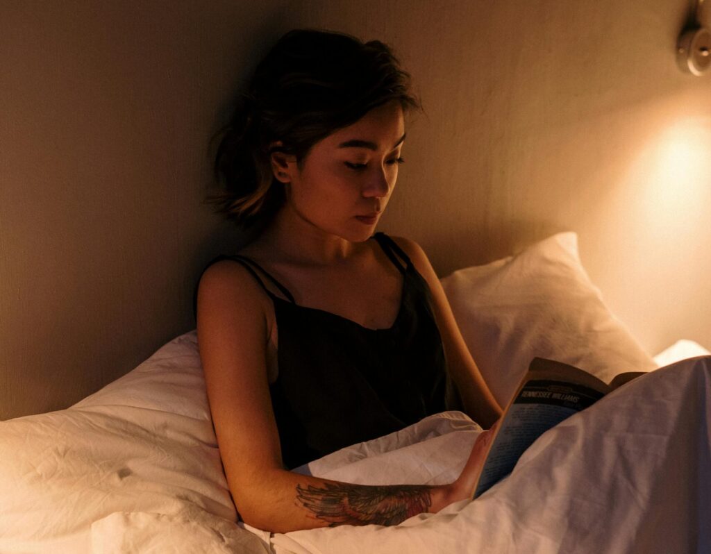 woman reading a book in bed under a tungsten light glow
