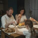 Family holding hands and praying over a dinner table with turkey and cookies during festival celebration.
